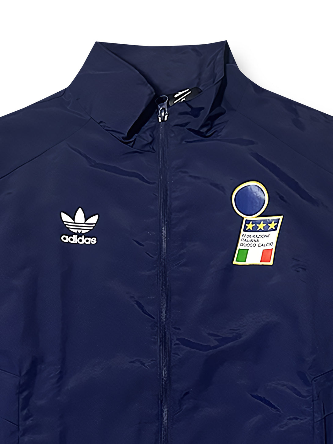 詳細画像1：胸元に配置された高品質刺繍のイタリア代表エンブレムとAdidasトレフォイルロゴのクローズアップ。ワールドカップ準優勝時代のクラシックなスタイルを表現。
詳細画像2：袖部に施されたグリーン・ホワイト・レッドの国旗三色ストライプデザインの特写。イタリアの民族性とサッカー文化を強調したディテール。
詳細画像3：袖口と裾部分の仕上げディテールのクローズアップ。軽量防風素材を採用し、快適性と実用性を兼ね備えたデザイン。