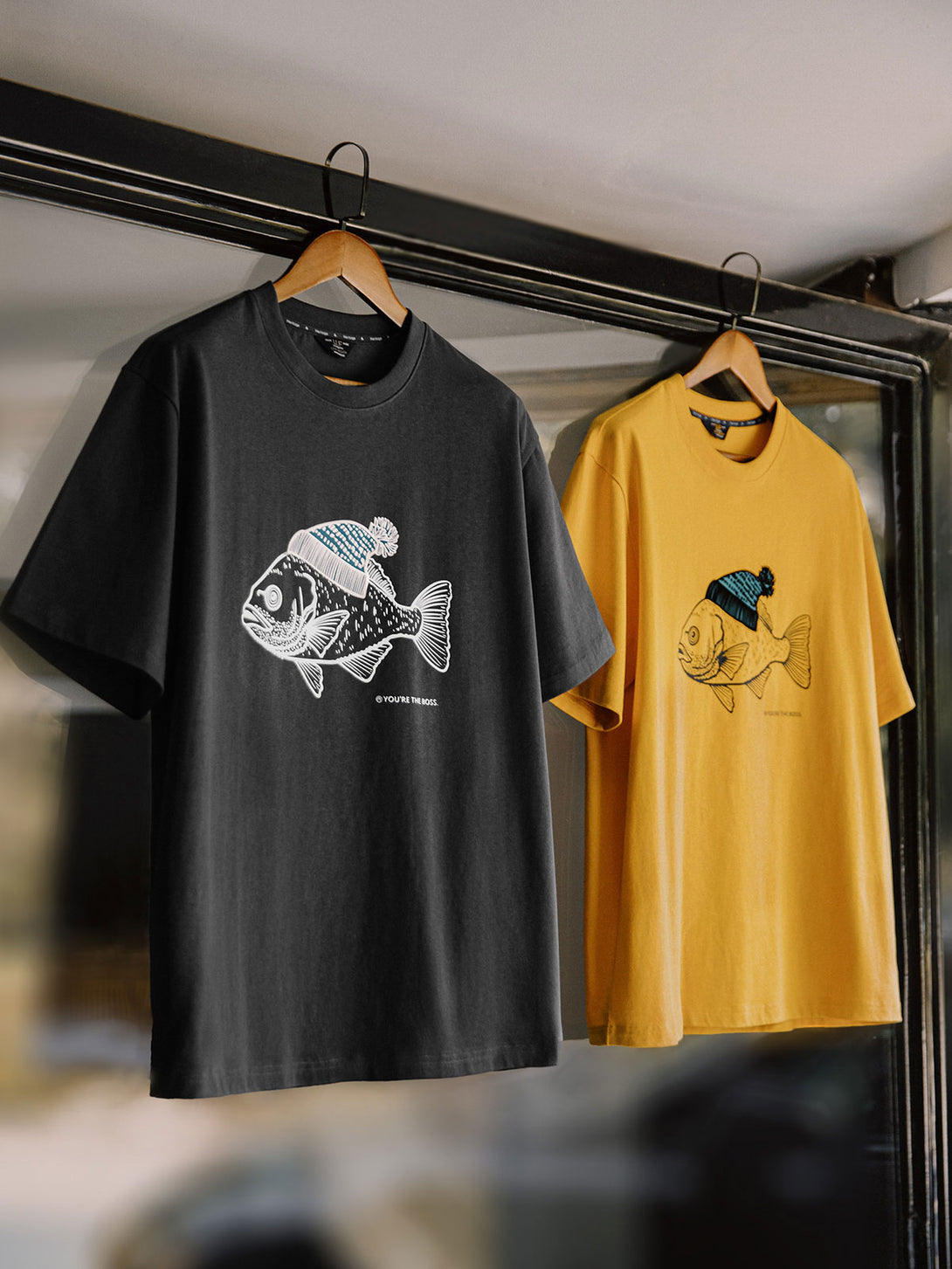 黄色の背景に帽子をかぶった深海魚のフロックプリントが施されたコットンTシャツの正面ビュー。しっかりした質感と優れた通気性を持つ純綿素材を使用しています。この代替テキストは、画像の内容を具体的に伝え、視覚情報にアクセスできないユーザーにも適しています。