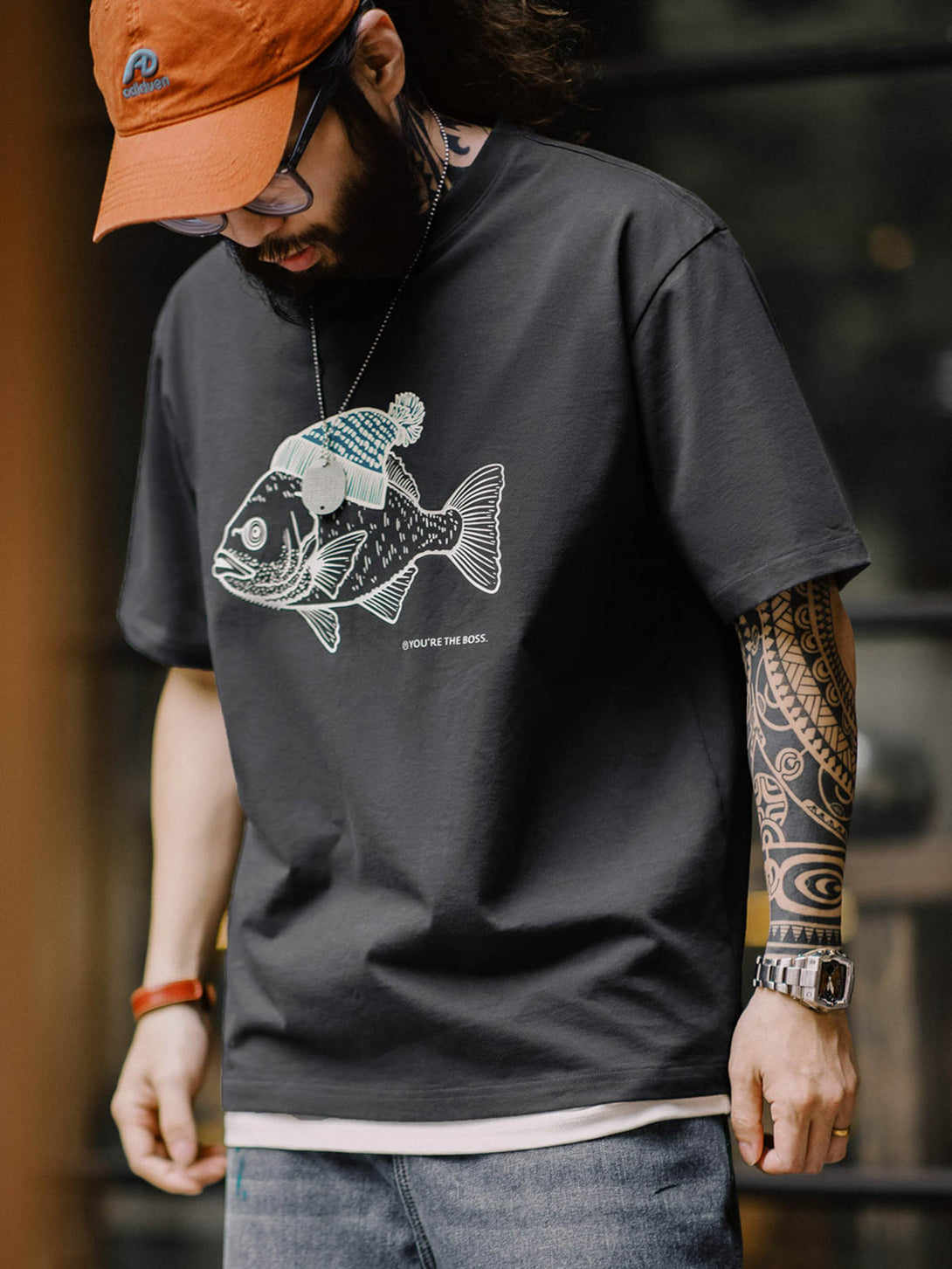 モデルがグレーの深海魚フロックプリントコットンTシャツを着用し、カジュアルパンツとスニーカーでスタイリング。リラックスフィットが週末のリラックススタイルを提案します。