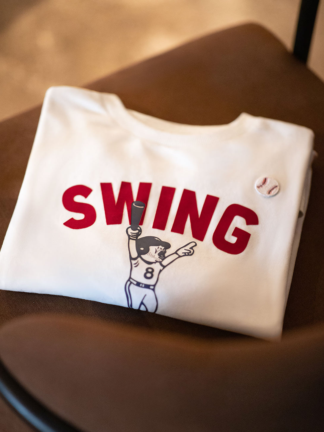 アメリカンカレッジスポーツスタイルのロングスリーブTシャツ、前面には大胆な「SWING」とバッティング姿勢のグラフィックがプリントされています。