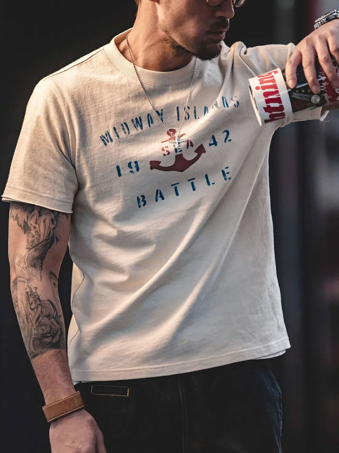 モデルが錨と「BATTLE」のプリント入りTシャツを着用し、ルーズなデニムパンツとシンプルなシューズでスタイリング。カジュアルで自然体のスタイルを演出しています。